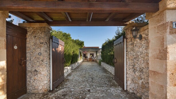 A stone-paved pathway leading to a rustic building with wooden doors and a stone wall. - Villetta Spiaggia Bella (Lecce)