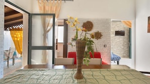 A modern living room with a large window, a wicker vase with flowers, a red sofa, and a brick wall. - Villetta Albachiara (Porto Cesareo)