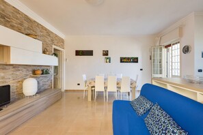 A modern living room with a blue sofa, a dining area with a table and chairs, and a kitchen area with a counter and cabinets.