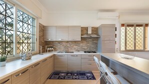 A modern kitchen with light wood cabinets, a stone backsplash, and a large window with a lattice design. - Villa Alessandra (Porto Cesareo)
