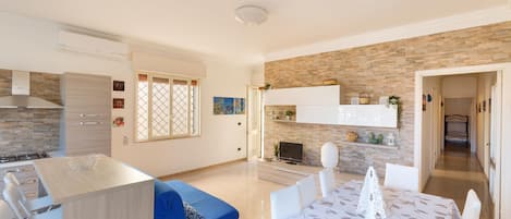 A modern kitchen with a dining area, featuring a kitchen island, a blue sofa, and a dining table with a floral tablecloth.