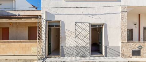 Un edificio moderno con dos puertas abiertas, una con reja metálica, y un pequeño balcón.