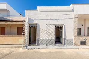 A modern building with two open doors, one with a metal gate, and a small balcony.