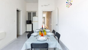 A dining area with a table set for six, chairs, a white tablecloth, and a colorful wall decoration. - Appartamento Giada (Porto Cesareo)
