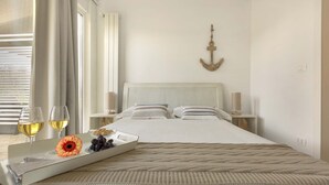 A neatly made bed with a beige blanket, a tray with a flower and grapes, and two glasses of white wine on the bedside table. - 1738 Tenuta degli Ulivi by Perle di Puglia (Melendugno)