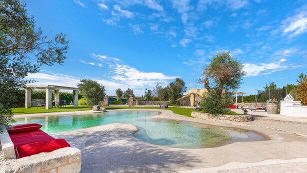 A swimming pool with a curved design, stone tiles, and a red bench. - 1738 Tenuta degli Ulivi by Perle di Puglia (Melendugno)