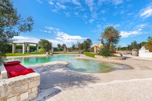 Una piscina con design curvo, piastrelle in pietra e una panca rossa.