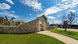 A stone archway leading to a covered area, surrounded by a stone wall and a grassy area with a paved path. - 1738 Tenuta degli Ulivi by Perle di Puglia (Melendugno)