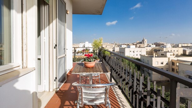 Een balkon met een tafel en stoelen, een bloempot en uitzicht op de stad.
