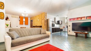 Una sala de estar moderna con sofá, alfombra roja, espacio de cocina con electrodomésticos y televisor.