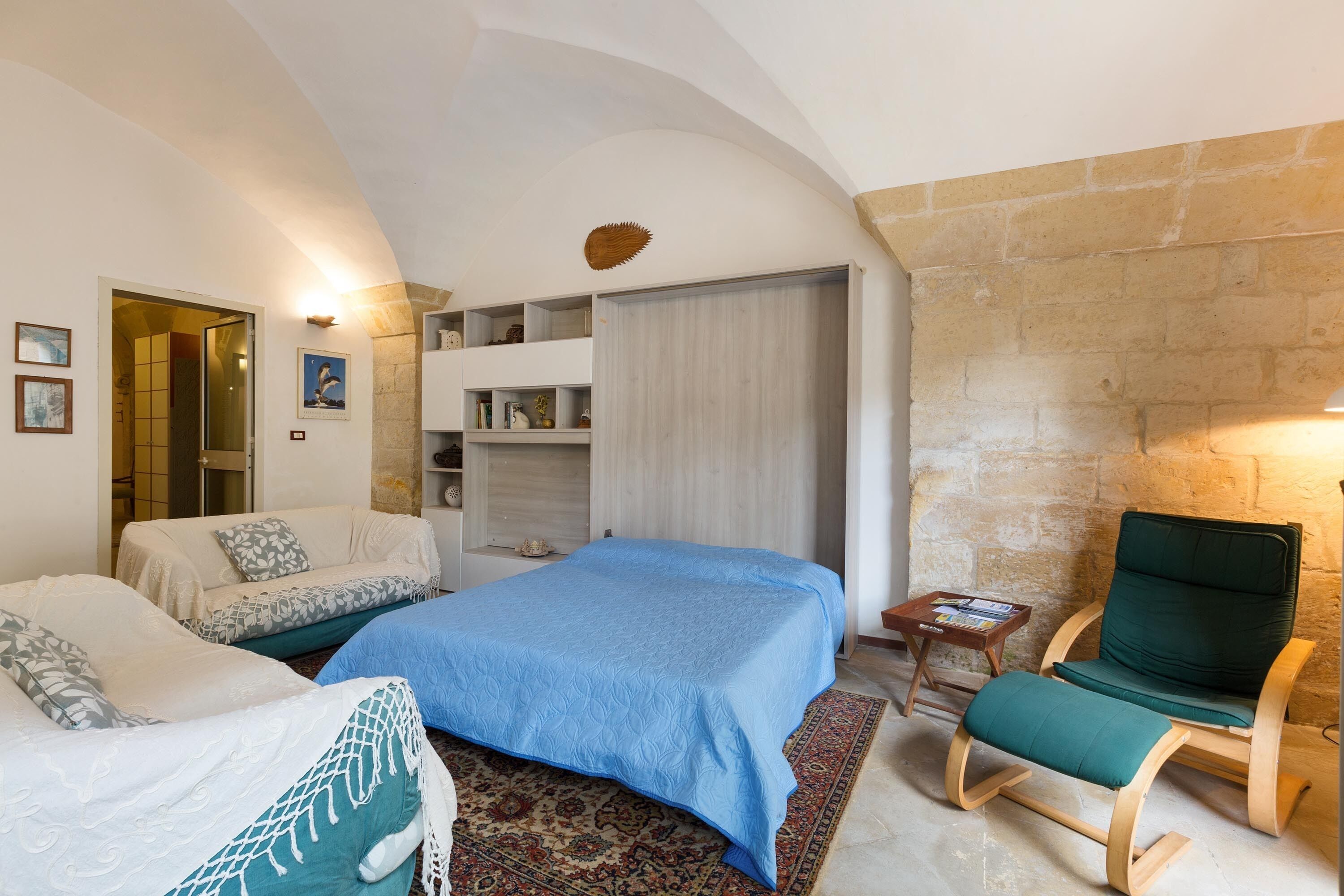 A bedroom with two beds, a wooden chair, a small table, and a stone wall.