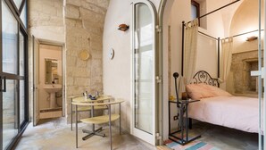 A bedroom with a bed, a glass shower enclosure, a small round table with chairs, and a bathroom with a sink and mirror. - Appartamenti Ai Fiorentini (Lecce)