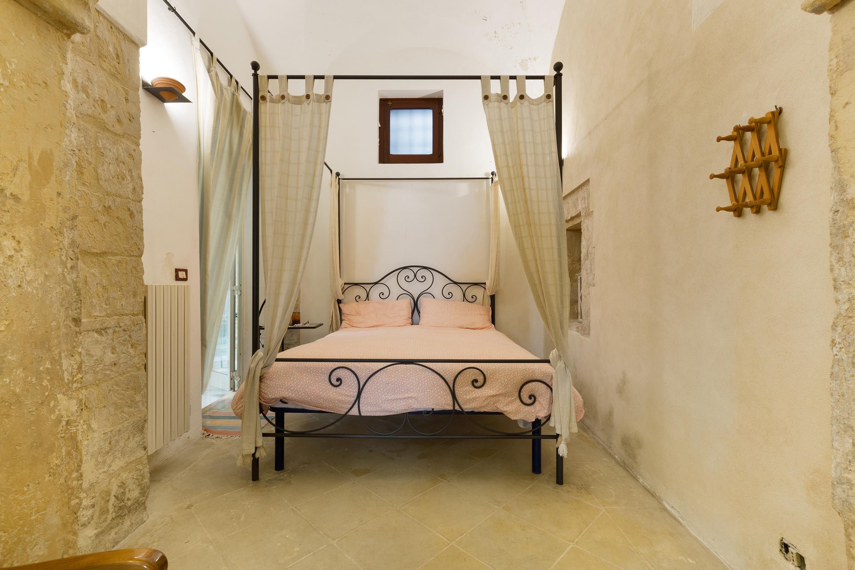 A four-poster bed with a headboard, a small window above, and a wall-mounted wooden rack.