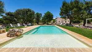 A rectangular swimming pool with clear water, surrounded by a stone deck and a grassy area with lounge chairs. - Villa Thea Charming House (Carovigno)