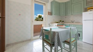 Een keuken met een tafel gedekt voor twee personen, een raam met uitzicht op palmbomen en groene kasten.