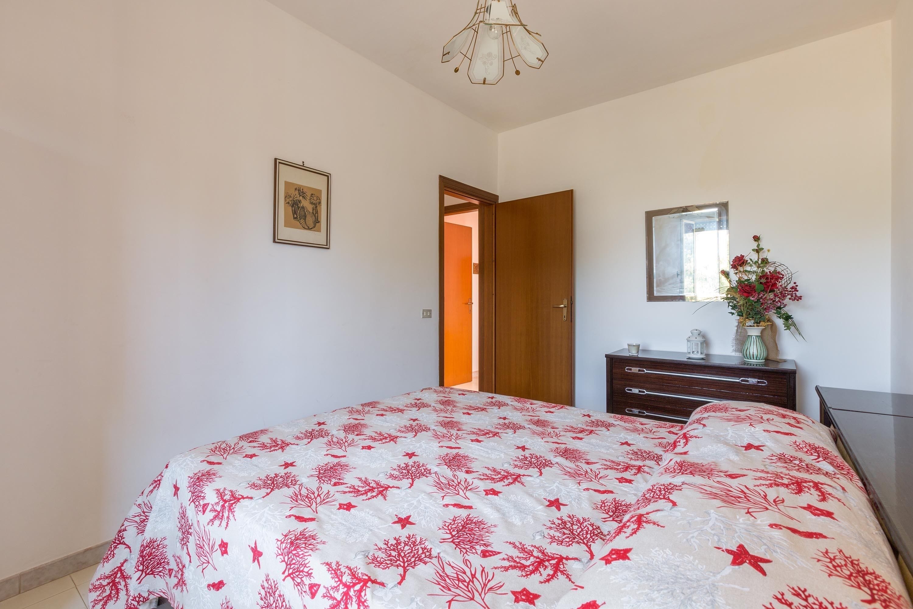 A bedroom with a bed, dresser, mirror, and a door leading to another room.