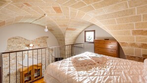 A bedroom with a stone ceiling, a bed with a white comforter, a wooden dresser, and a small window. - La Nicchia di Luana (Copertino)