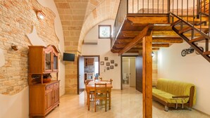 A spacious living area with a wooden dining table, a sofa, and a staircase leading to an upper level. - La Nicchia di Luana (Copertino)