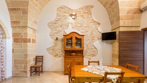 A dining area with a brick wall, wooden cabinet, and a TV mounted on the wall. - La Nicchia di Luana (Copertino)
