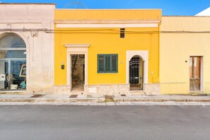 Um edifício amarelo com fachada de pedra, uma entrada pequena e uma janela com persianas verdes.