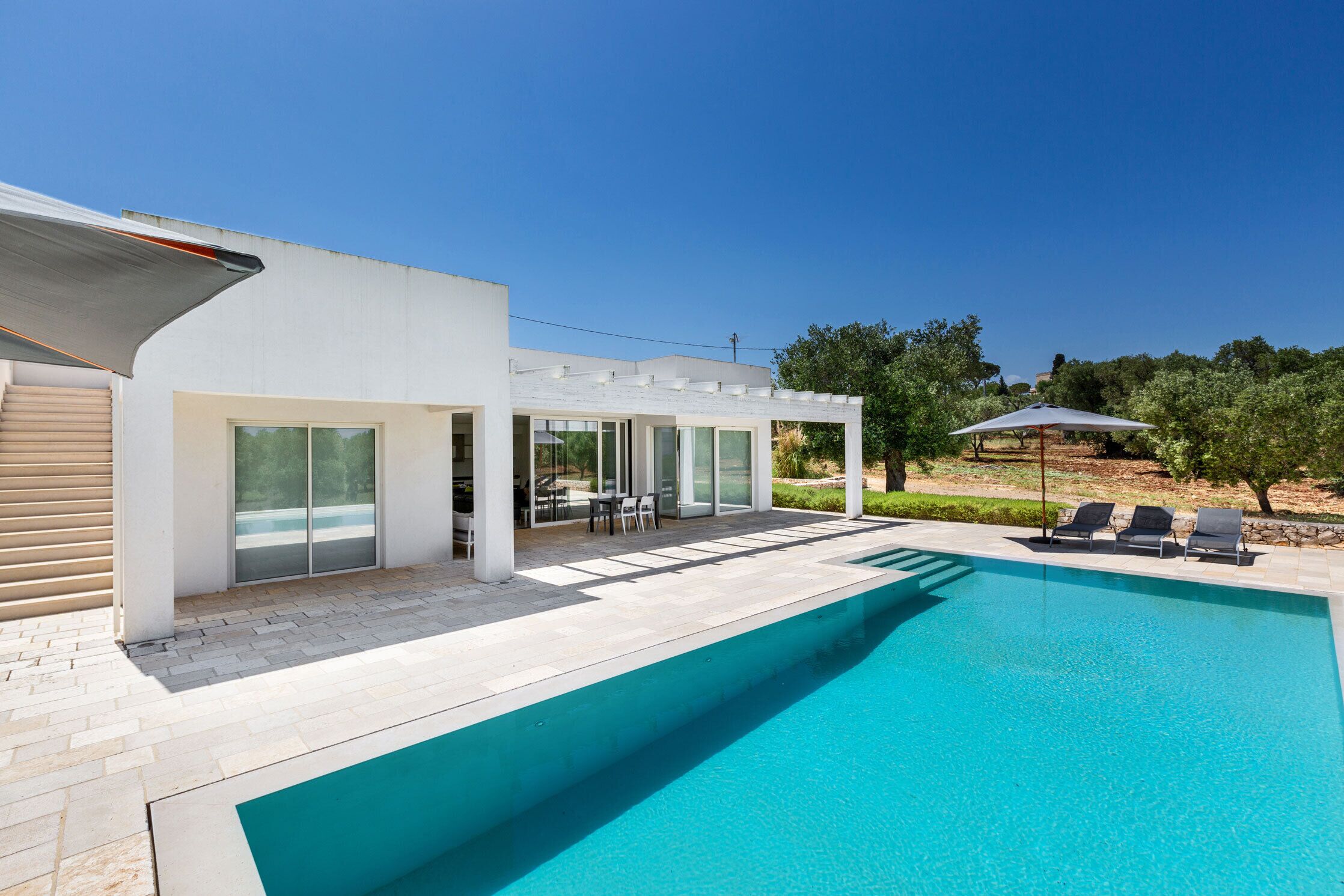 Una casa moderna con piscina, mobiliario de exterior y una pérgola.