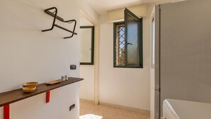 A narrow hallway with a white refrigerator, a wooden shelf with bowls, and a window with a view of trees.