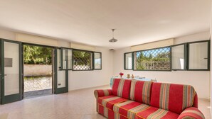 A spacious room with a red sofa, a dining table with chairs, and a view through open doors to an outdoor area.