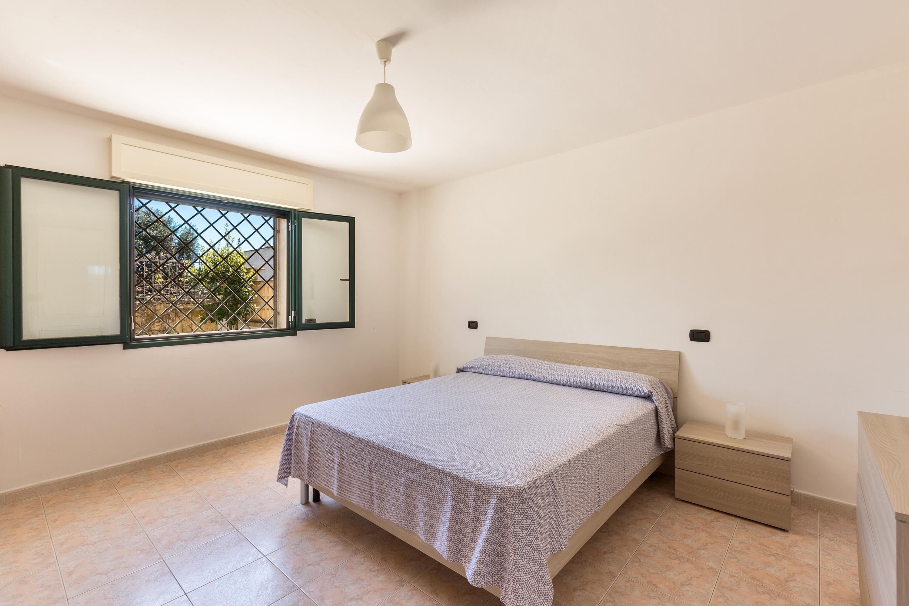 Um quarto com uma cama, uma mesa de cabeceira, uma janela com vista e uma luminária no teto.