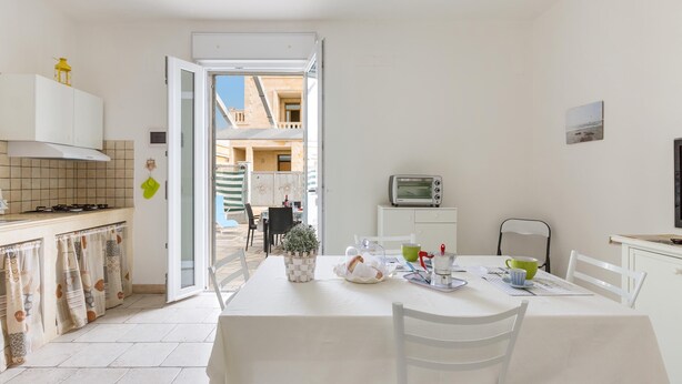A bright kitchen with a dining area, a TV, and a view of a courtyard. - Casa Medusa (Torricella)