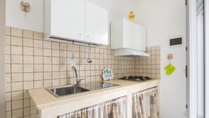 A kitchen with white cabinets, a stainless steel sink, a gas stove, and a tiled backsplash. - Casa Medusa (Torricella)