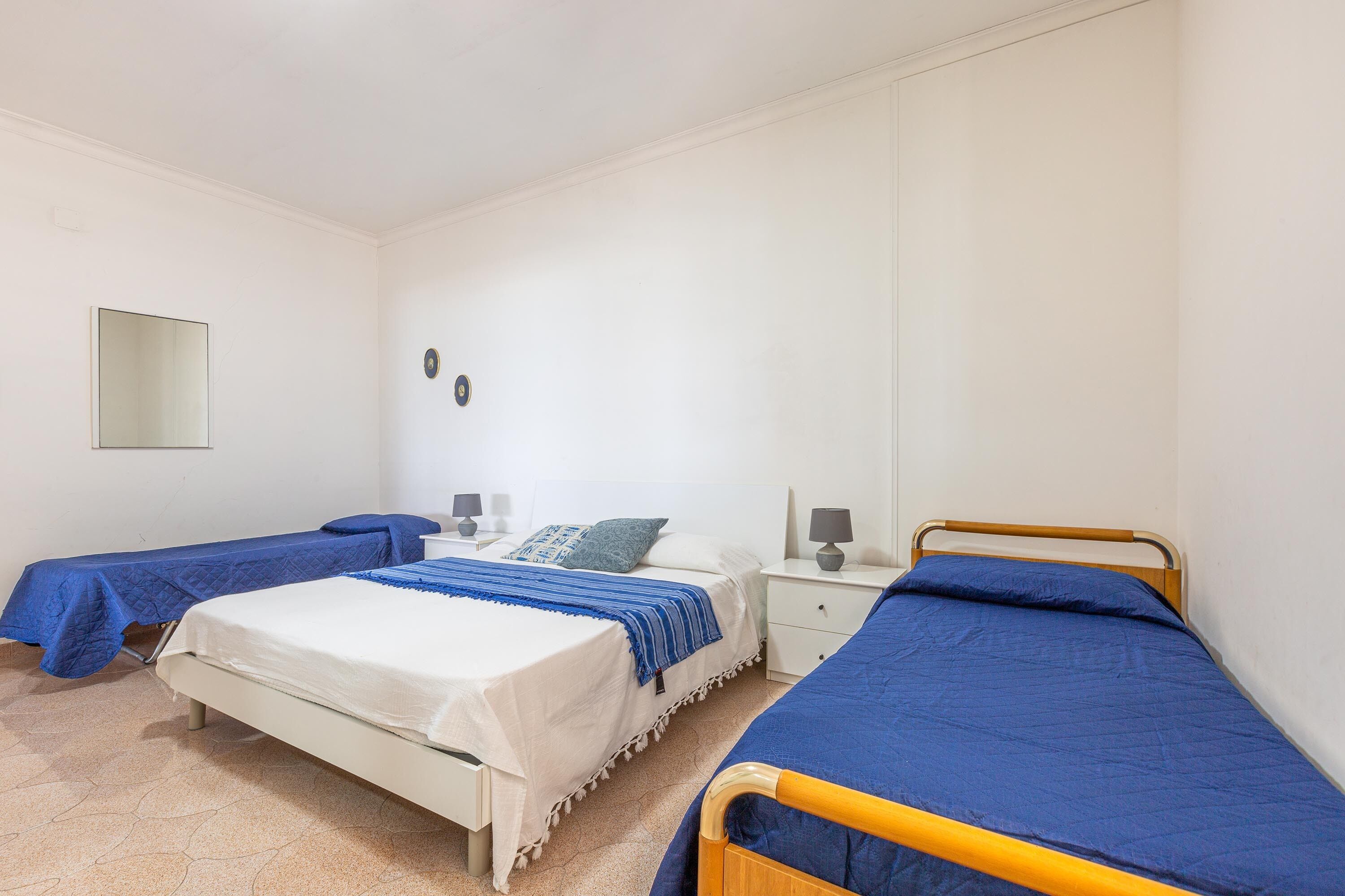 Ein Schlafzimmer mit zwei Betten, jeweils mit blauer Bettdecke, einem Nachttisch mit Lampe und einem an der Wand befestigten Spiegel.