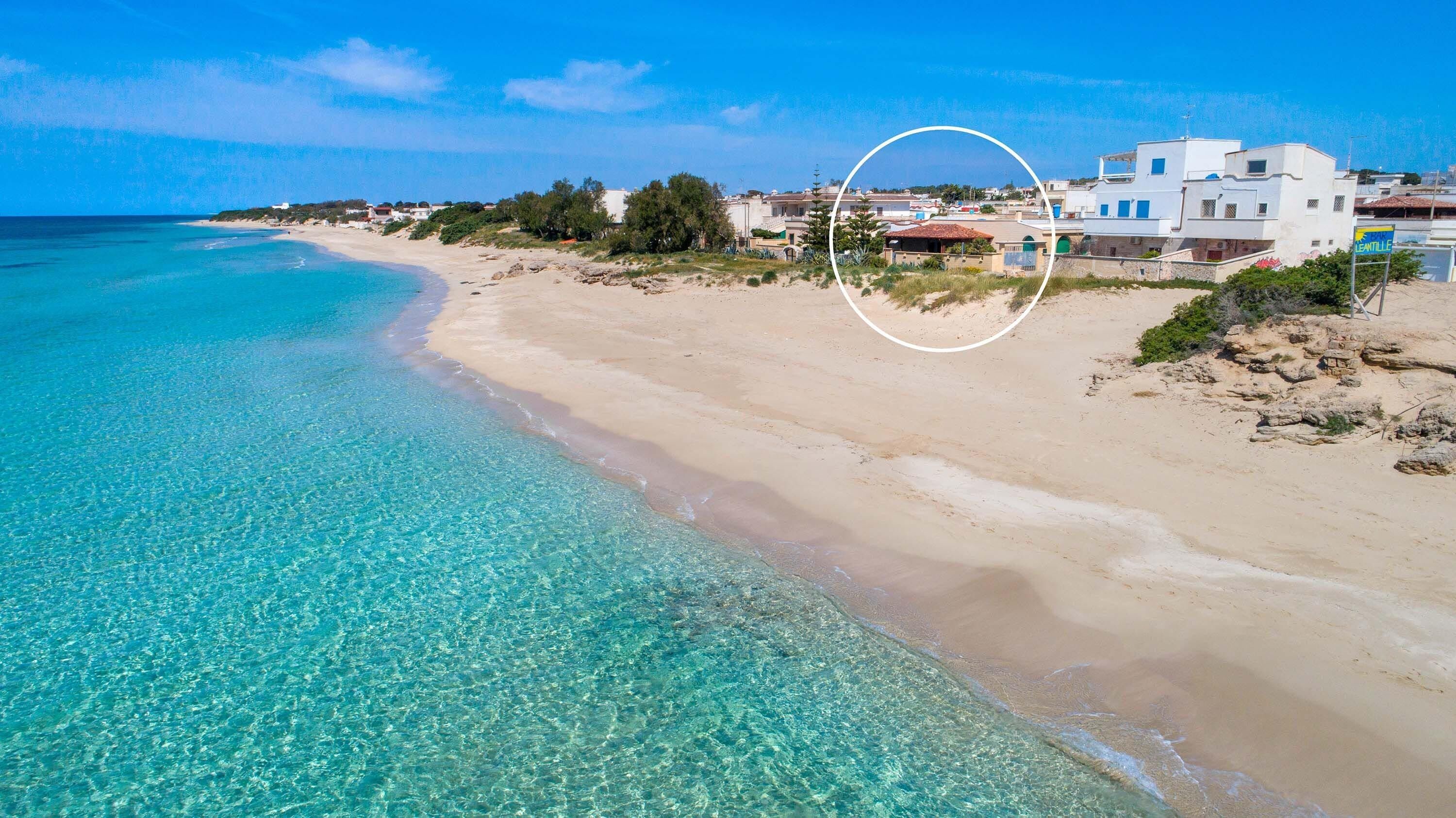 A beach with clear turquoise waters, sandy shore, and a white building with a blue sign.