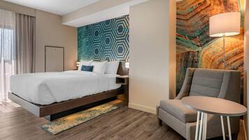 A modern hotel room with a large bed, a seating area with a small table, and a decorative wall with geometric patterns.