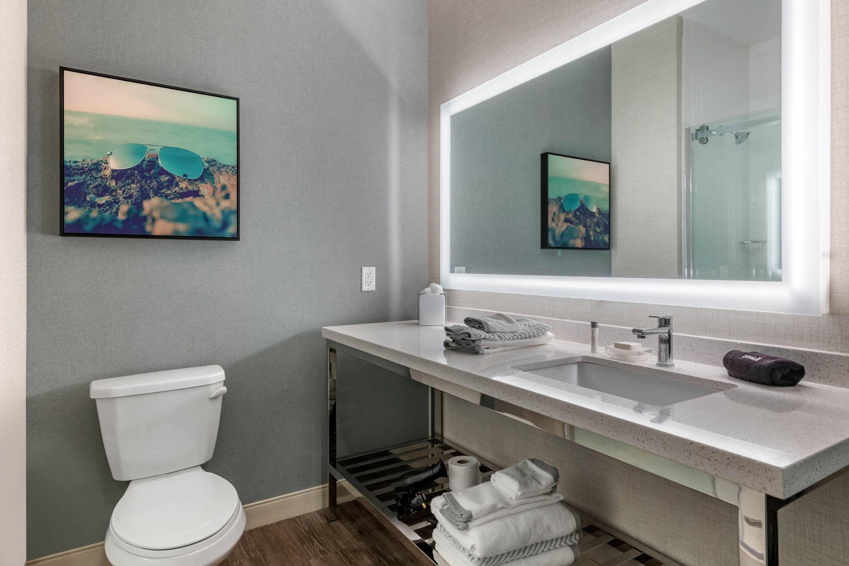 A modern bathroom with a white toilet, a sink with a mirror, and a framed picture on the wall.