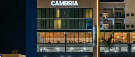 A multi-story building with a prominent 'CAMBRIA' sign, featuring a modern design with large windows and a covered parking area.