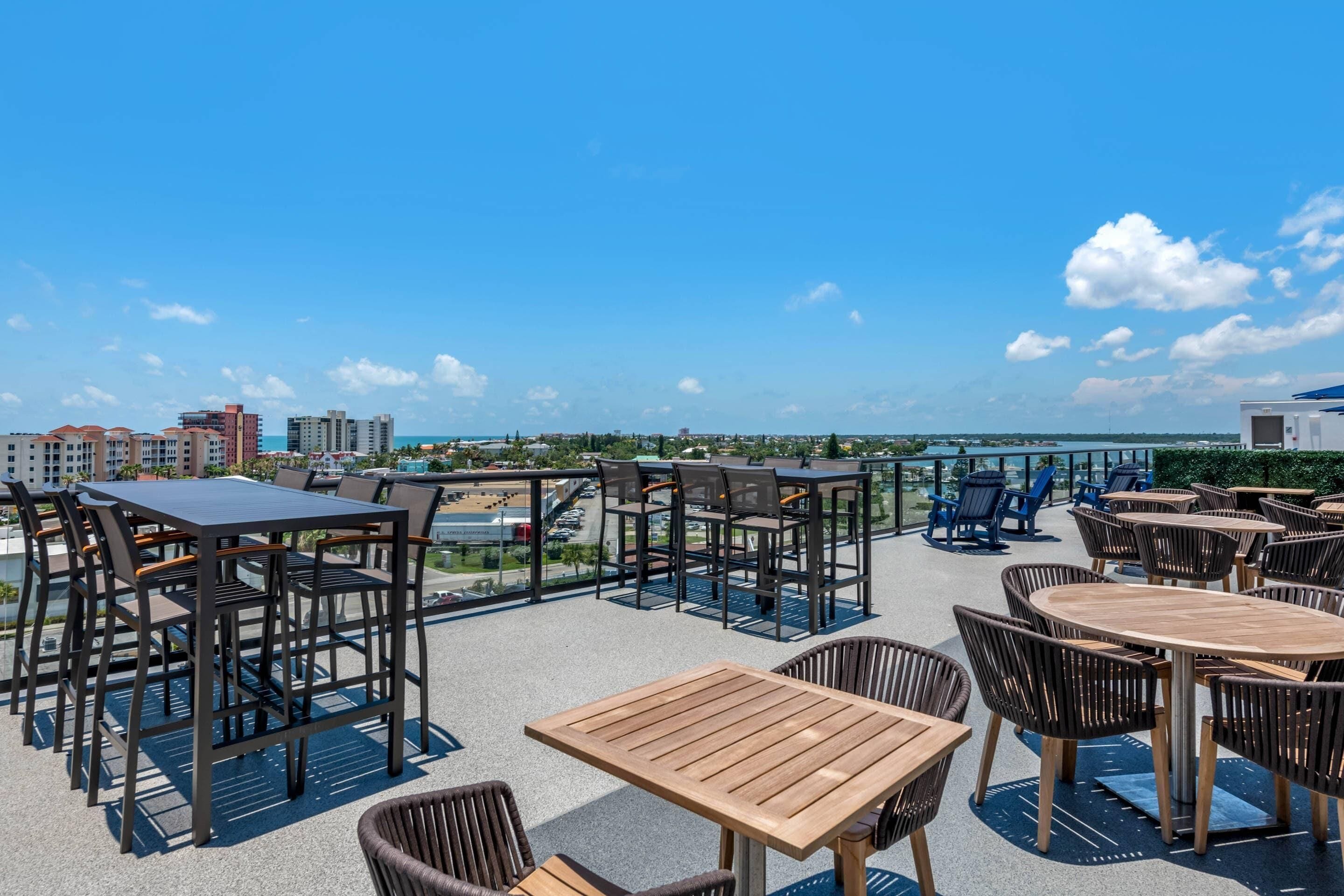 Une terrasse extérieure dotée de nombreuses tables et chaises, offrant une vue sur le paysage urbain et sur l’eau.