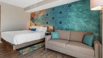 A hotel room with a bed, a sofa, a nightstand, and a wall with a geometric pattern.