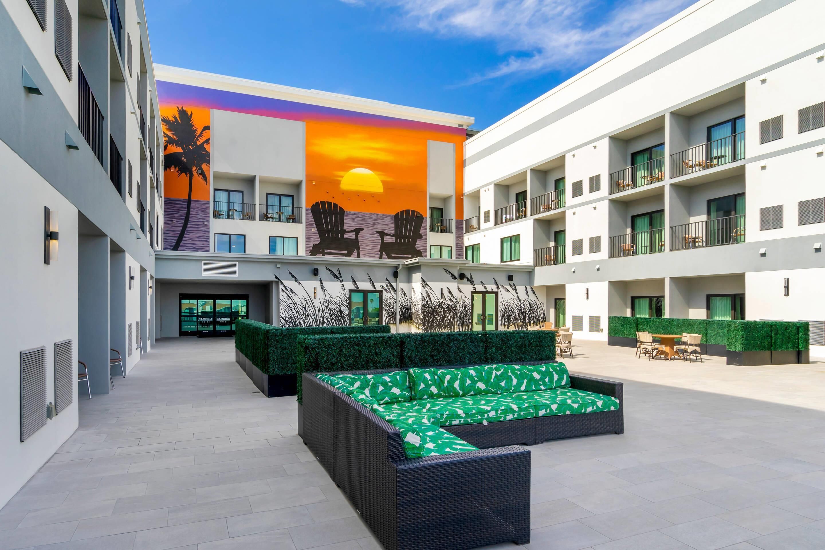 Een moderne hotelbinnenplaats met een groot terras, een muurschildering van een zonsondergang en meerdere balkons.