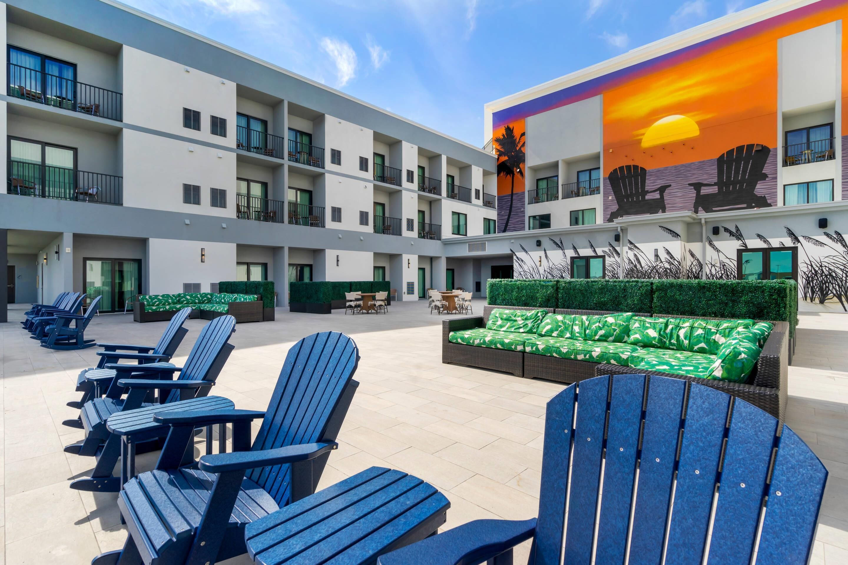 A hotel courtyard with outdoor seating, a mural of chairs, and a green lawn.