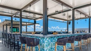 An outdoor bar area with a tropical-themed tiled backsplash, multiple bar stools, and a clear view of the sky. - Cambria Hotel St Petersburg-Madeira Beach Marina (Madeira Beach)