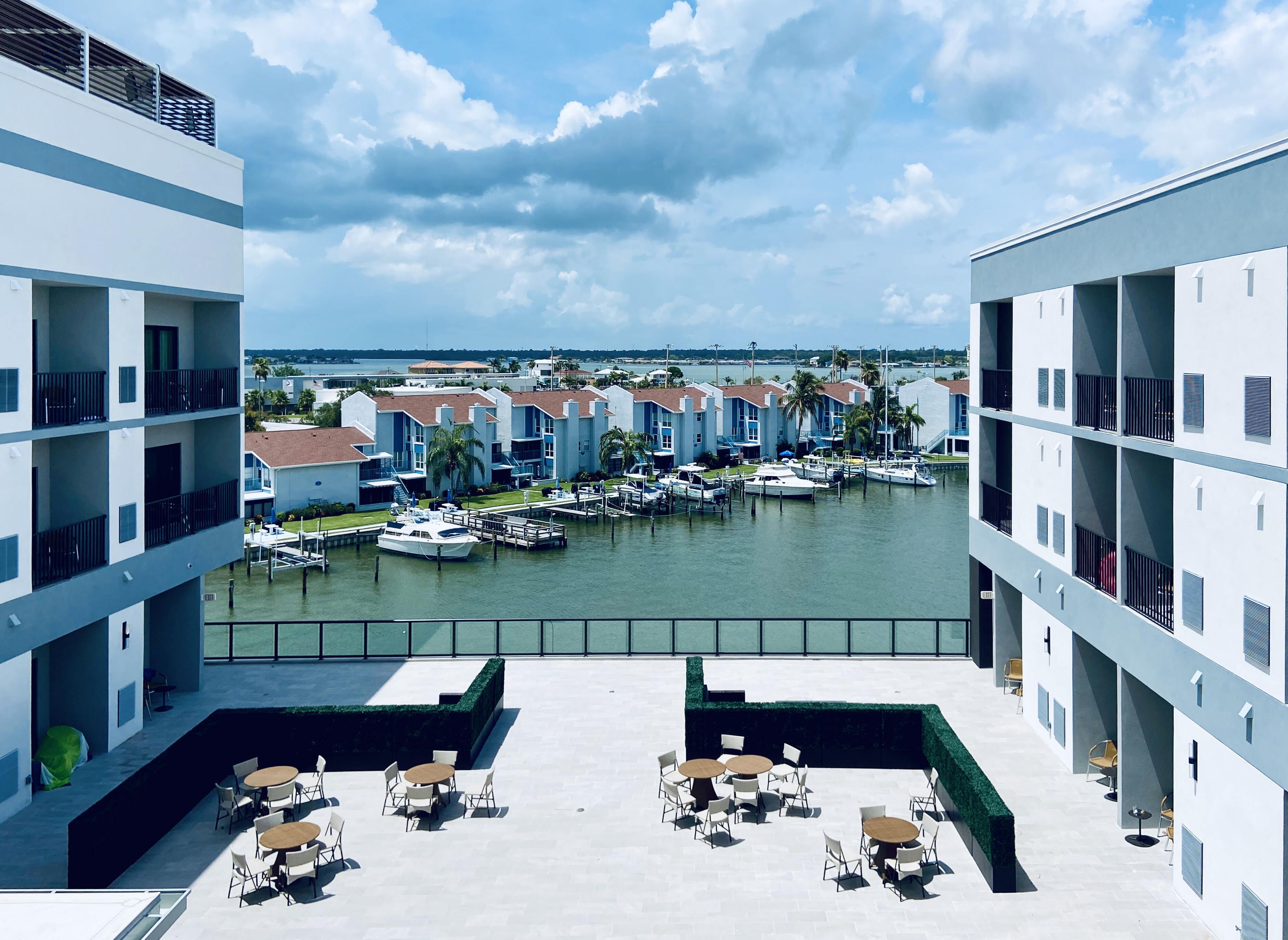 Un puerto deportivo con barcos amarrados, vista al agua y un edificio con varios balcones y mesas al aire libre.