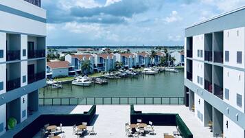 A marina with boats docked, a waterfront view, and a building with multiple balconies and outdoor seating.