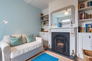 A living room with a white sofa, blue rug, fireplace, bookshelves, and a mirror. - Captains Cottage, a delightful, bright & airy, period property located just a few minutes from the b (Deal)