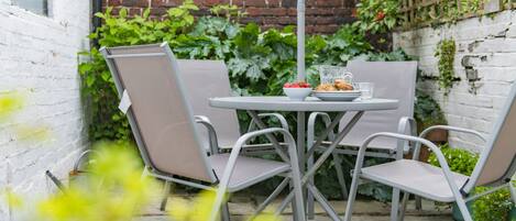 A patio with a round table and four chairs, surrounded by greenery and a brick wall.