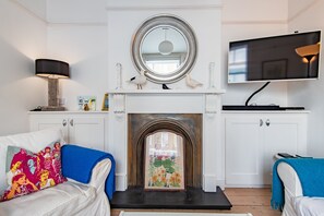 A room with a fireplace, a television, and two blue sofas. - Captains Cottage, a delightful, bright & airy, period property located just a few minutes from the b (Deal)
