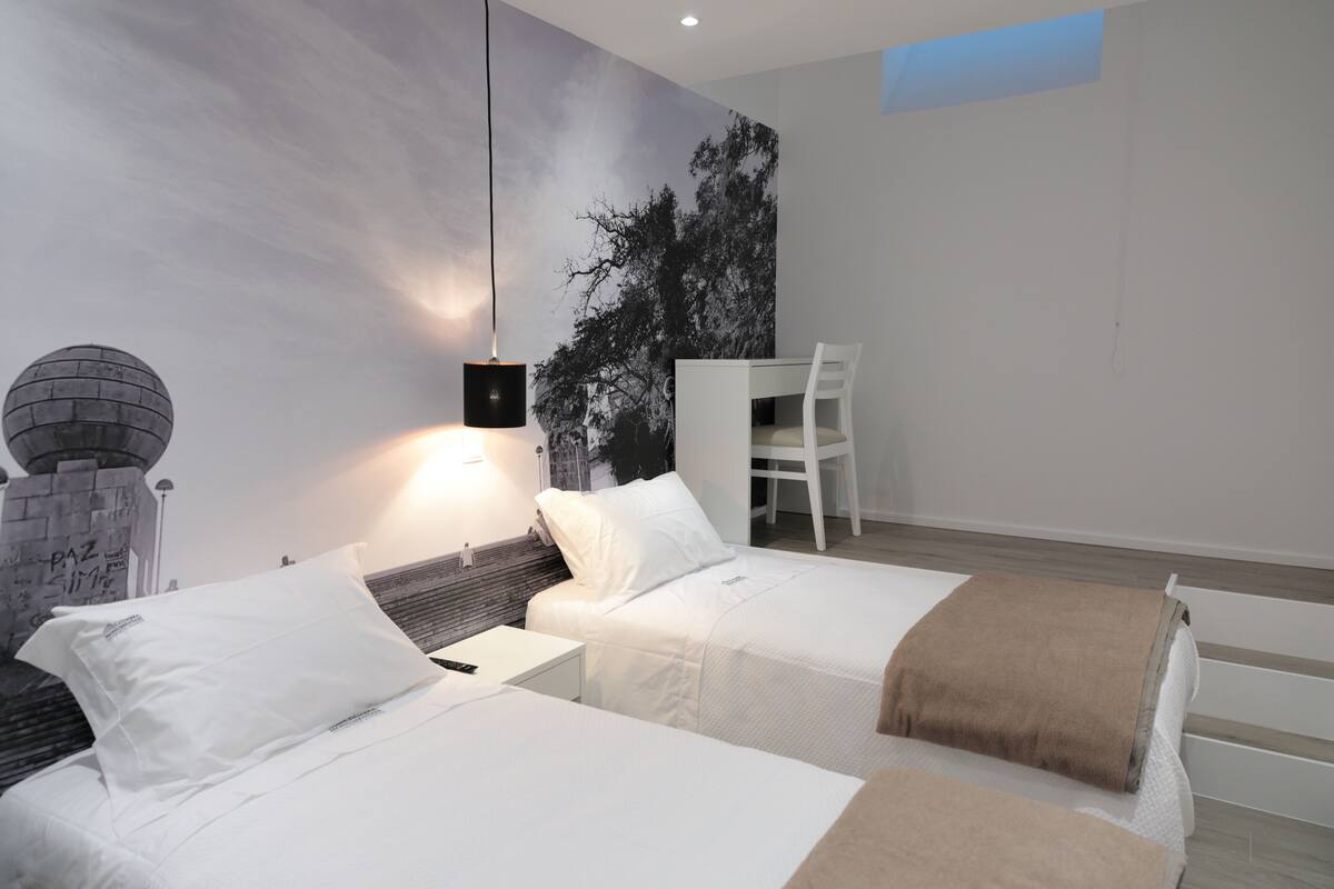 A modern hotel room with two beds, a desk, and a chair.