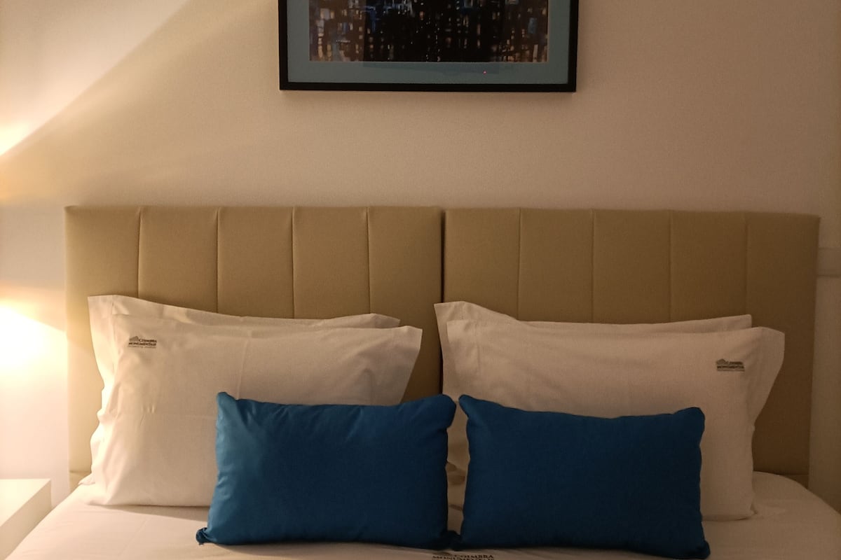 A hotel room with a bed, two pillows, a headboard, and a framed picture on the wall.