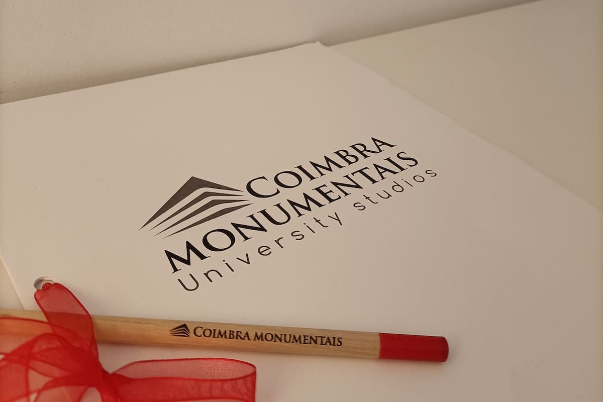A white certificate with the logo and name 'COIMBRA MONUMENTAIS' and 'University Studies' printed on it.