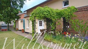 A house with a garden, a brick wall, and a white door. - Landhaus Chlosta (Biendorf)
