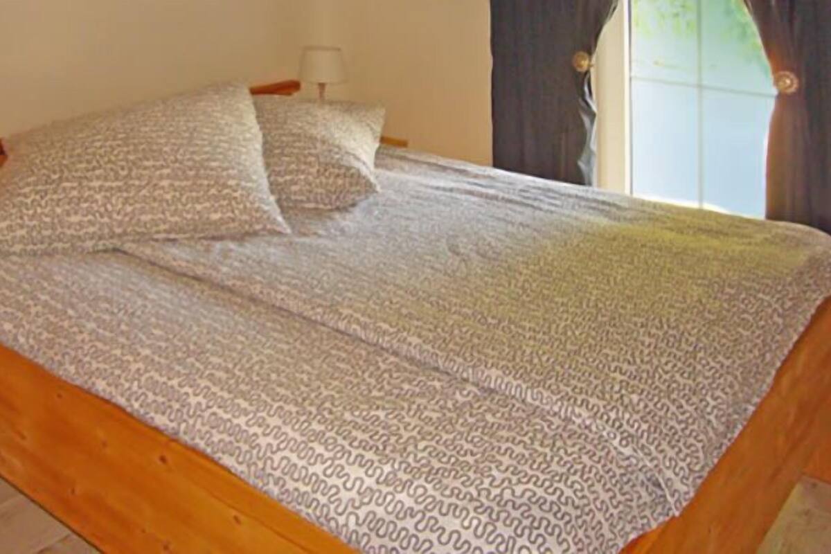 Una cama de madera con ropa de cama estampada, una mesita de noche con lámpara y una ventana con cortinas.